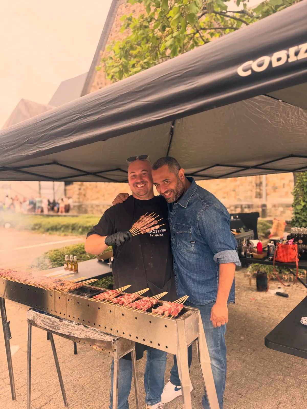 Mario met een gast onder de tent, aan de grill
