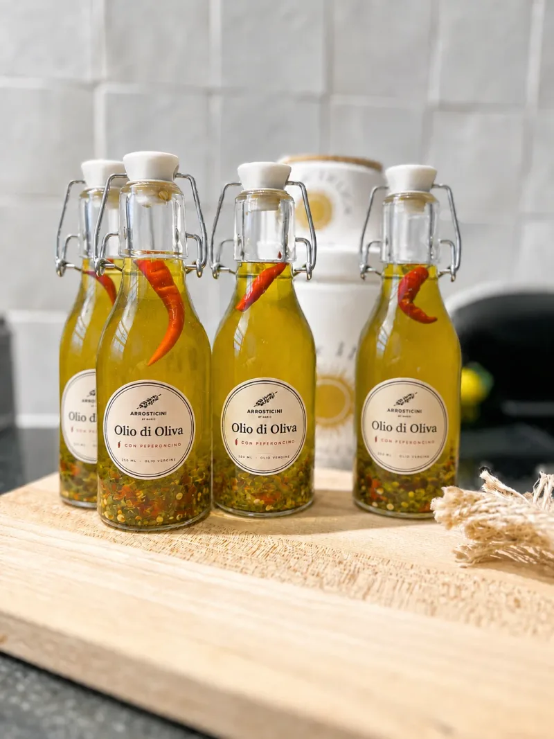Quattro bottigliette di olio d’oliva piccante fatto in casa, con i peperoncini, su un tagliere di legno